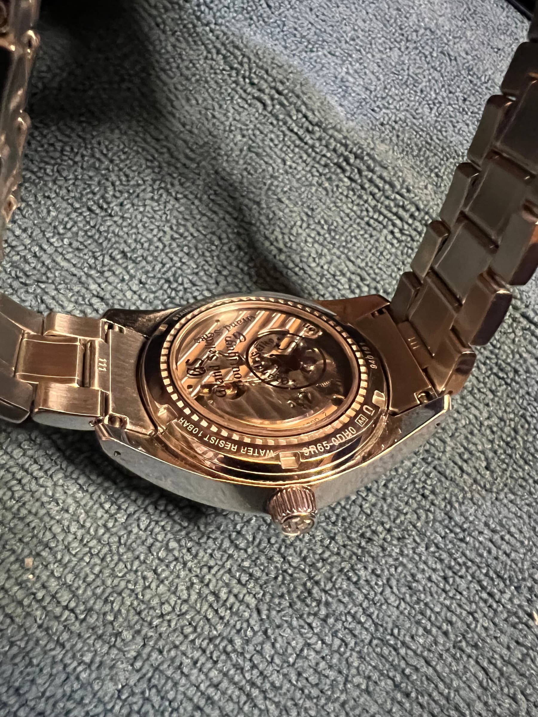 The display caseback and bracelet, the 9R65 movement visible through the sapphire and the finishing catching the light