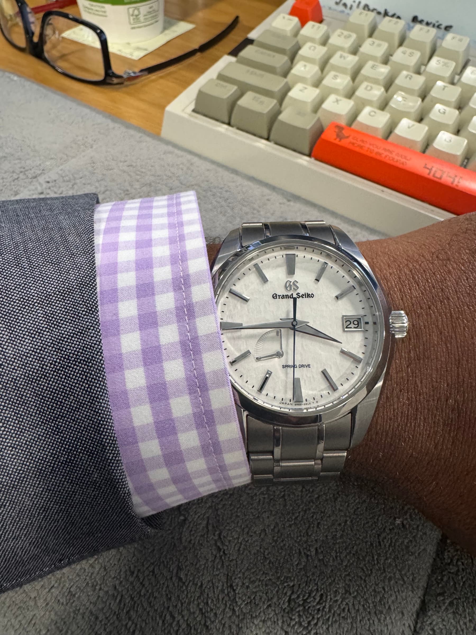 A Grand Seiko SBGA211 Snowflake on the wrist, its textured silver-white dial and blued seconds hand catching the light above a lilac gingham shirt cuff.