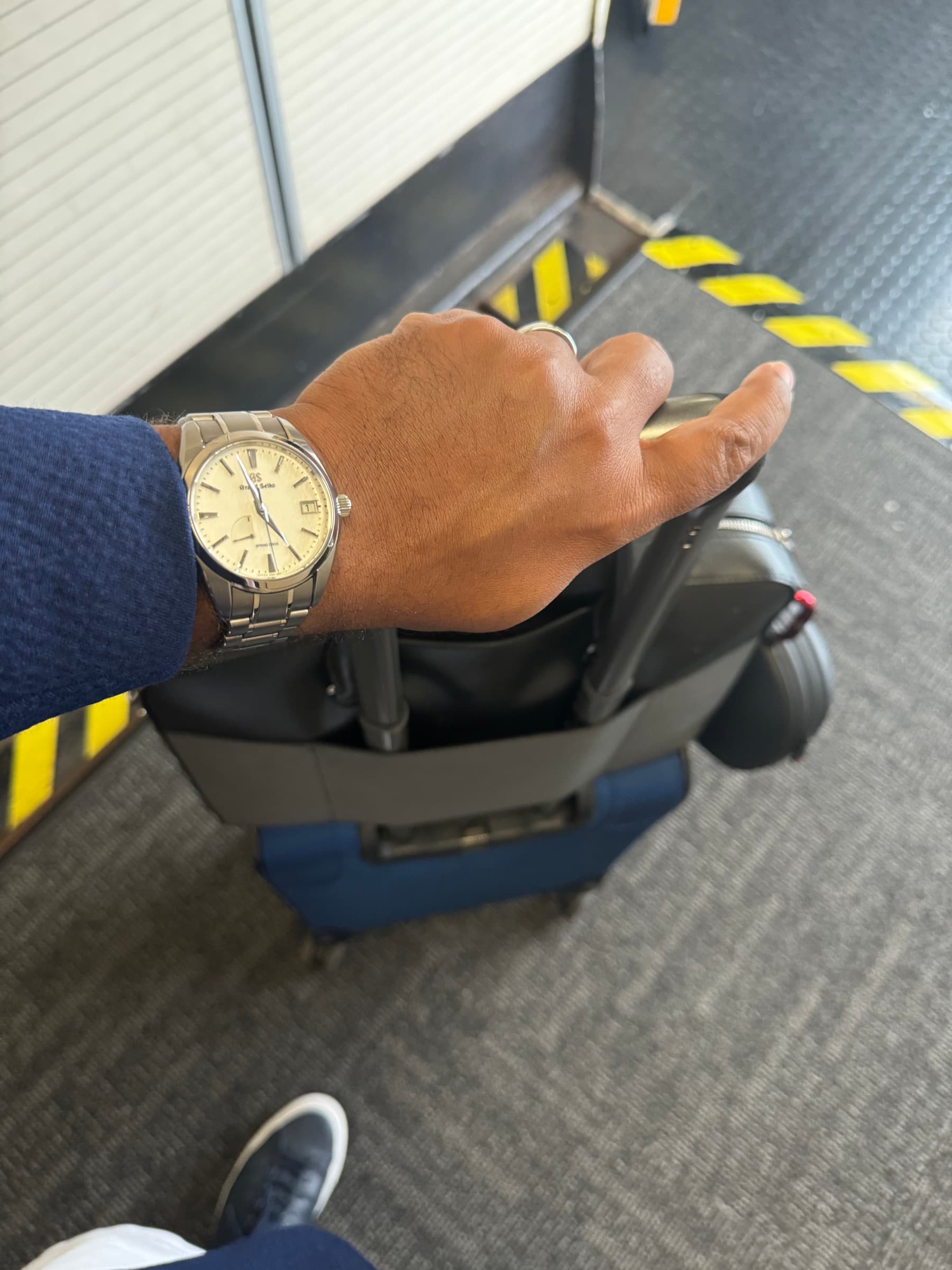 On the wrist while traveling, sleeve pushed back, the Grand Seiko catching airport light